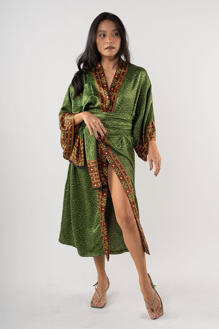 Woman wearing a green dress with patterned trim on a white background